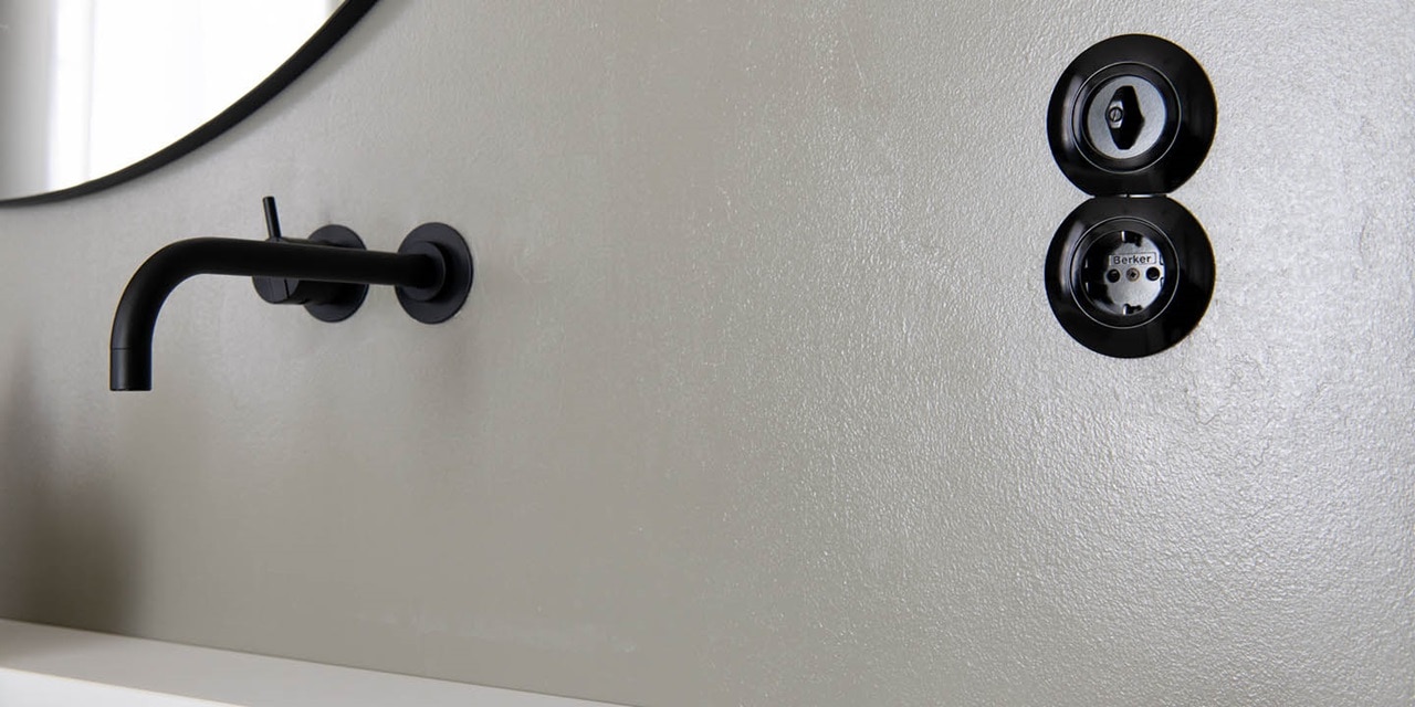 Moderne schwarze Wandsteckdose und Lichtschalter an grauer Wand montiert