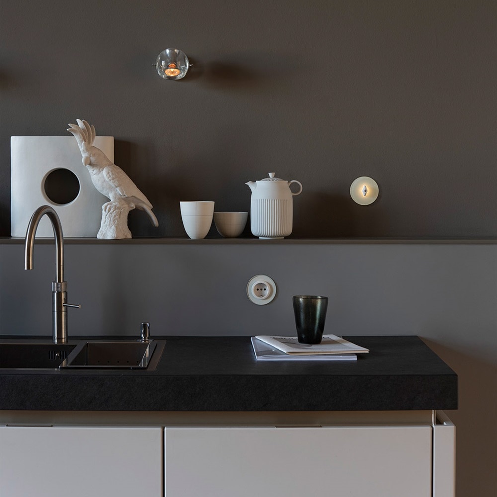 Beispiel einer Installation Berker Serie Glas Lichtschalter mit beleuchtetem Knebel und Abdeckplatten aus Glas auf grauer Wand oberhalb Spüle