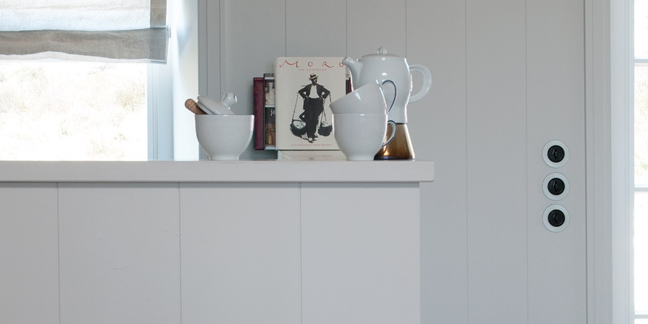 Modernes Kücheninterieur mit einem Regal für Utensilien und Bücher sowie einer Reihe von ordentlich angeordneten schwarzen Wandsteckdosen