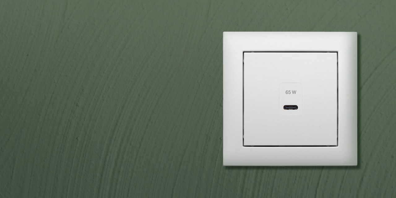 Weiße wandmontierte USB-C-Steckdose mit einer Leistungsbewertung von 65 W an einer grünen Wand