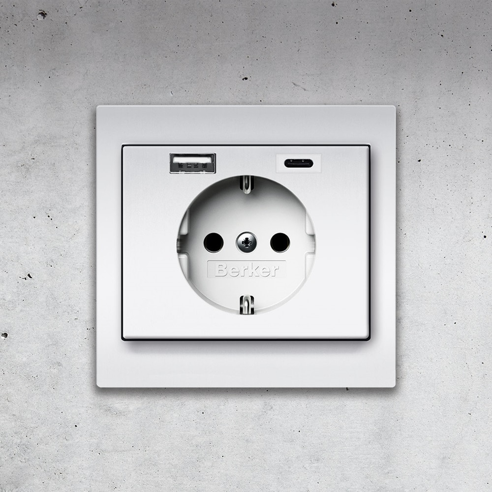 Frontalansicht Berker K.5 Steckdose mit 2-fach USB-Ladedose (1x USB-A, 1x USB-C) und Rahmen aus Aluminium auf Betonwand