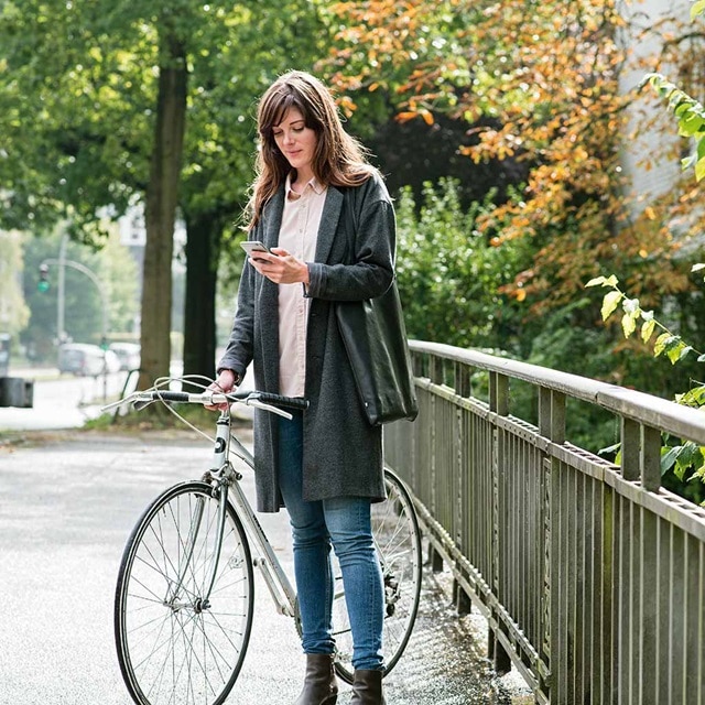 Person mit Fahrrad überprüft ein Smartphone auf einem Stadtbürgersteig