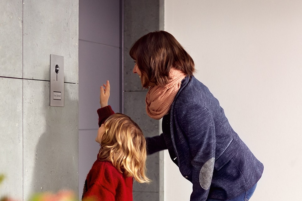Erwachsene und Kind bedienen einen modernen Hager Lichtschalter an einer Betonwand