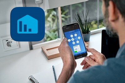 Mann an Schreibtisch der auf Smartphone mit App für Energiemanagement schaut