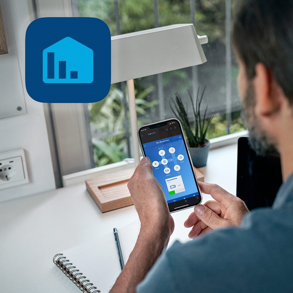 Mann an Schreibtisch der auf Smartphone mit App für Energiemanagement schaut