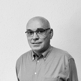 Schwarzweißes Foto von Franz Kinzel, Frontalansicht vor Wand mit Rauhfasertapete