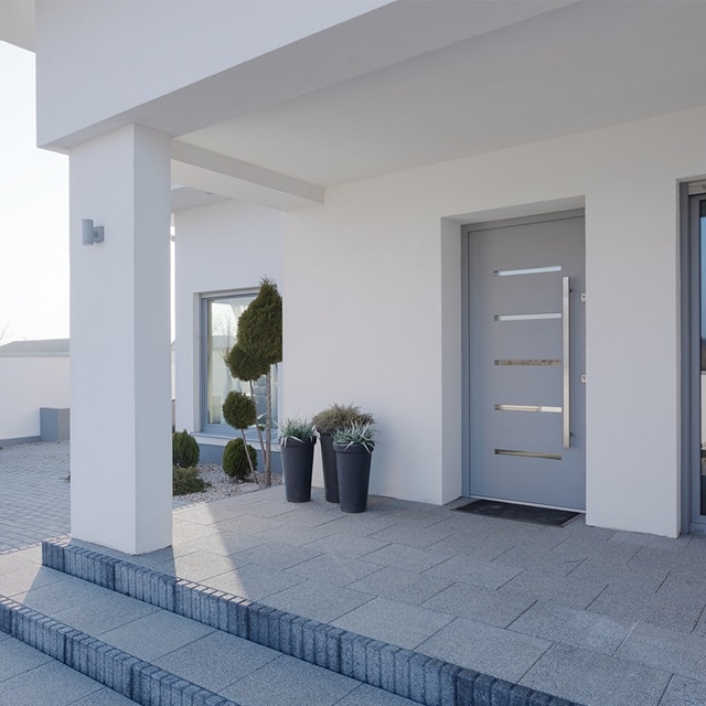 Blick auf Eingangsbereich eines modernen Wohngebäudes mit grauer Eingangstür, Überdachung und Pflanzen