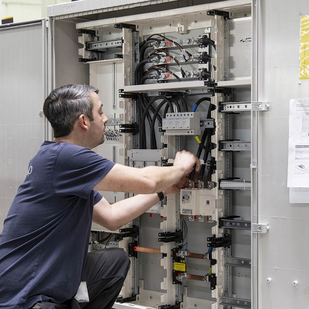 Schrägansicht Elektriker vor Hager Wanderschrank (Tür nach links und rechts geöffnet) bei Montage elektrischer Leiter