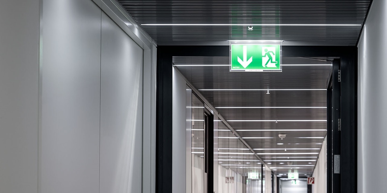 Moderner Büroflur mit beleuchtetem LED-Notausgangsschild in Grün über der Tür