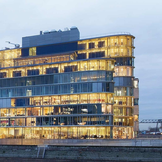 Modernes Bürogebäude bei Dämmerung erleuchtet mit sichtbarer Innenbeleuchtung und mehreren Stockwerken