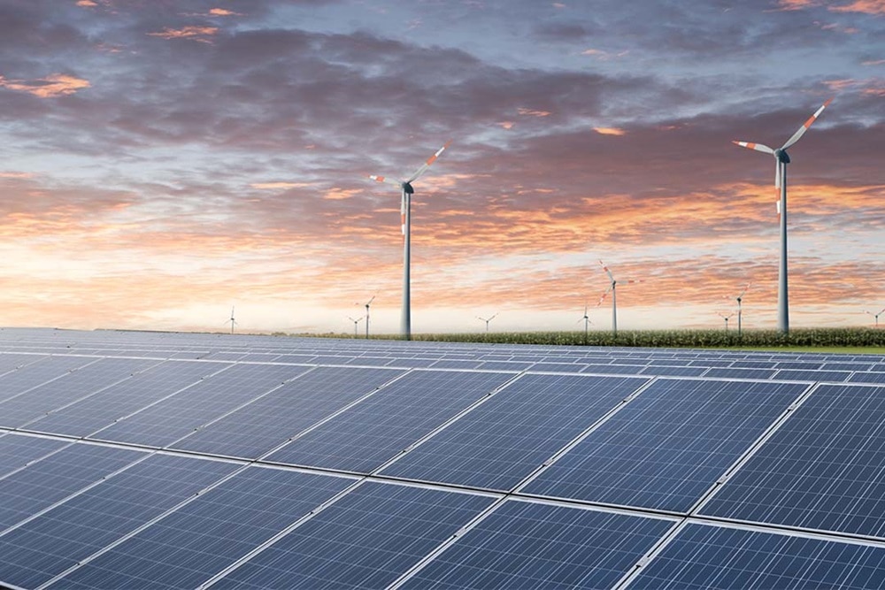 Blick in Landschaft am Abend mit PV-Feld im Vordergrund und Windrädern im Hintergrund