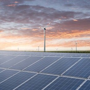 Blick in Landschaft am Abend mit PV-Feld im Vordergrund und Windrädern im Hintergrund