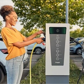 Lachende Frau, die Ladeskabel für das Elektroauto an die Hager Witty Park Ladesäule anschließt