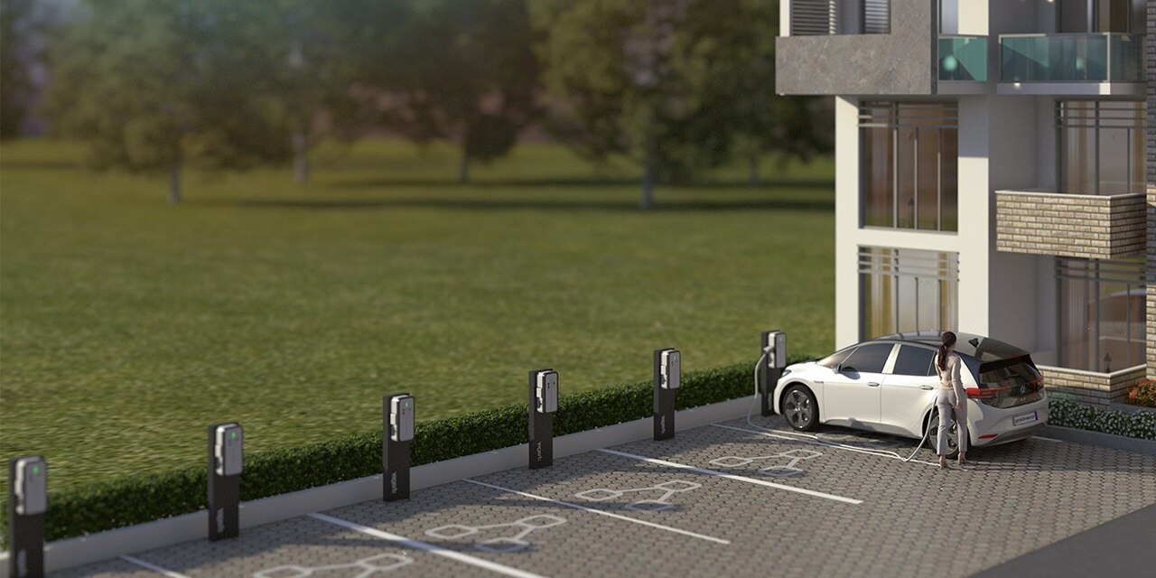 Mehrfamilienhaus mit Parkplatz mit mehreren Hager Witty Ladesäulen und Frau, die ihr Auto laden lässt