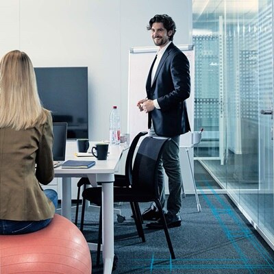 Blick in Büroraum mit Mann vor Flipchart, der einer Frau vor ihm zulächelt 