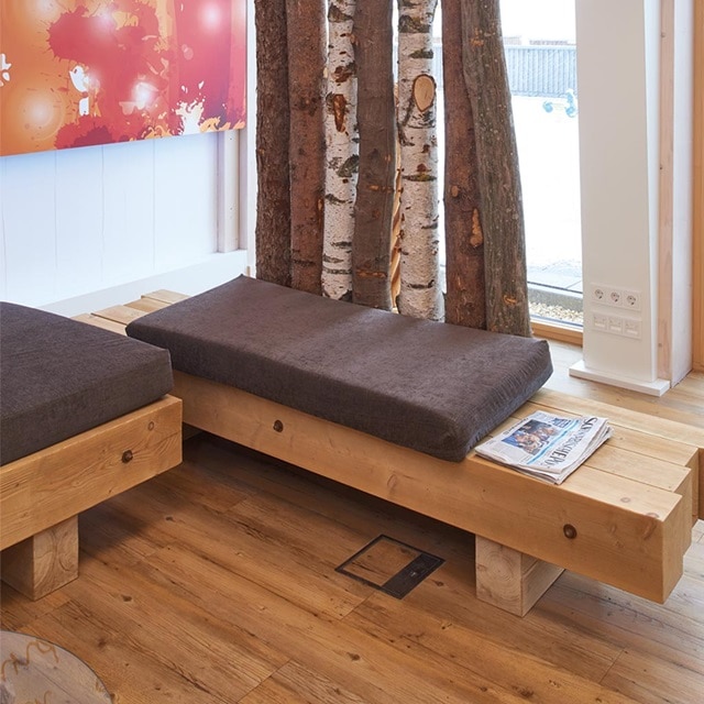 Innenansicht eines modernen Raumes mit einer Holzbank, Kissen, einer Bodensteckdose und Elektrosteckdosen an der Wand