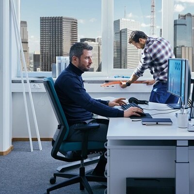 Blick in Büro mit Mann vor Schreibtisch, im Hintergrund werden Leitungen in einem Hager tehalit Brüstungskanal verlegt