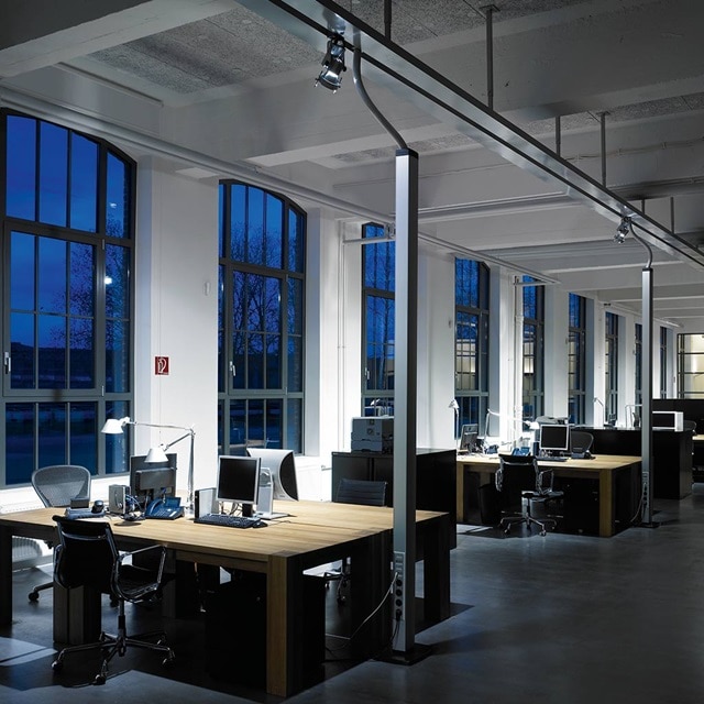 Modernes Bürointerieur mit Schienensystemen für Beleuchtung und Computerarbeitsplätzen in der Abenddämmerung