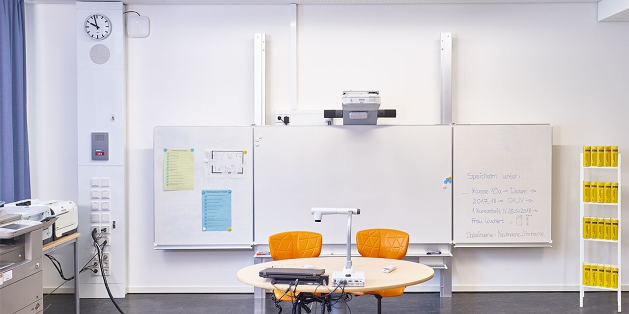 Modernes Besprechungszimmer mit Projektor, Whiteboards, rundem Tisch mit orangen Stühlen und Steckdosen an der Wand