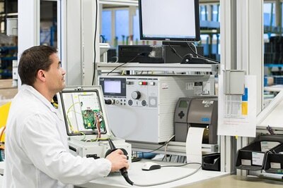 Blick in Hager Werkshalle mit Techniker an Tisch, der Messprüfung an technischem Gerät durchführt