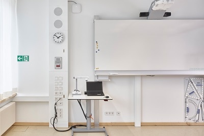Blick in Klassenraum mit üppig ausgestattetet Hager Mediensäule, Notebooktisch und Whiteboard mit Projektor