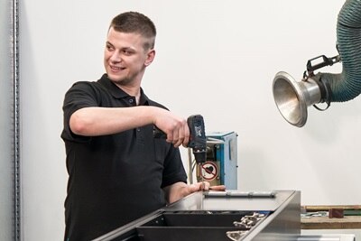 Blick auf Monteur, der mit Akkuschrauber Frontplatte mit integrierten Steckdosen an Hager Mediensäule befestigt