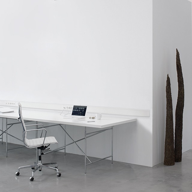 Modernes Büro mit weißem Schreibtisch, Stuhl, an der Wand montiertem Kabelkanal mit Steckdosen und Schaltern sowie dekorativer Skulptur