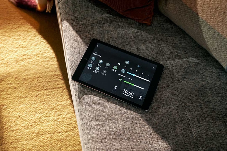 Smart-Home-Tablet mit Automatisierungssteuerungsschnittstelle auf einer Couch in einem Wohnzimmer