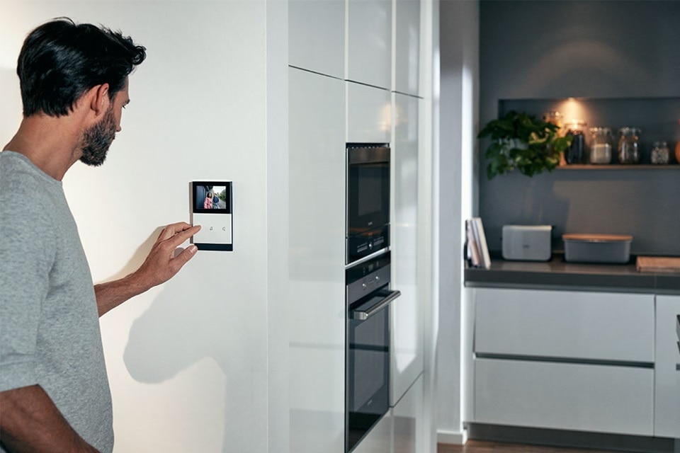 Person benutzt ein Smart-Home-Touchscreen-Panel in einer modernen Küche
