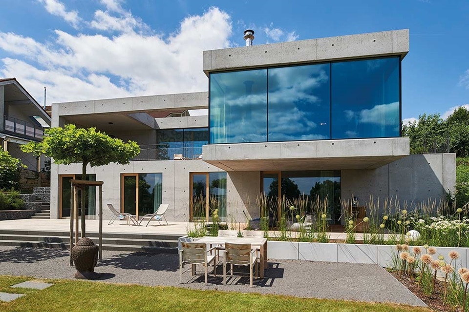 Modernes Haus aus Beton und Glas mit Gartenmöbeln und Landschaftsgestaltung
