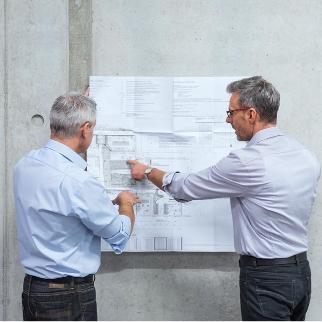 Zwei Fachleute besprechen einen Bauplan an einer Betonwand