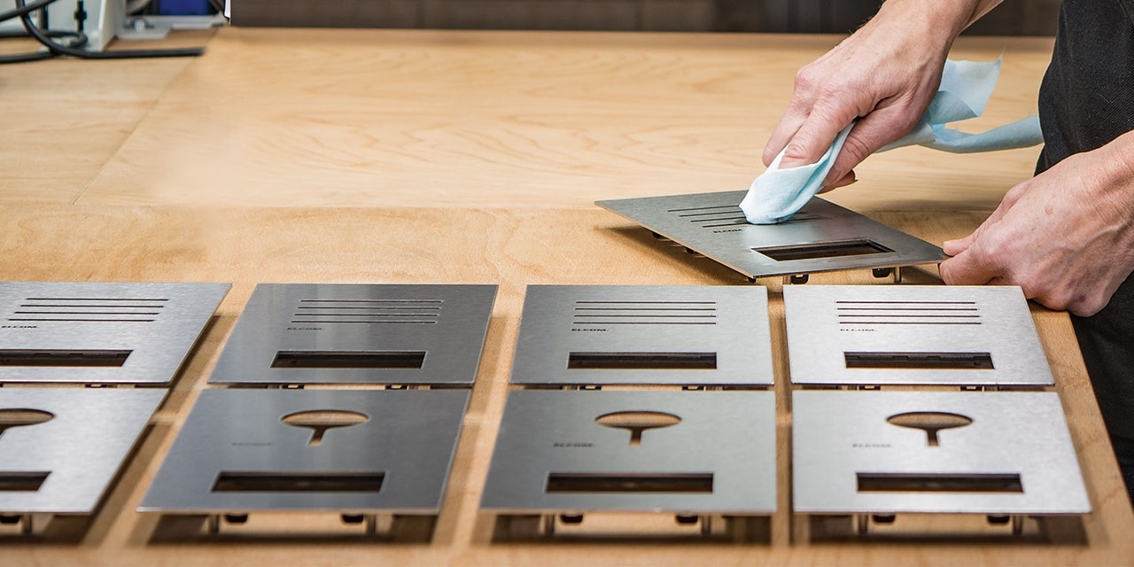 Person reinigt eine Auswahl an metallenen Abdeckungen für Elektrosteckdosen auf einem Holztisch