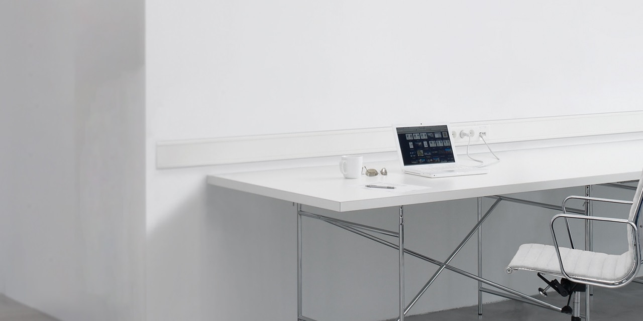Minimalistischer Büroraum mit Laptop auf dem Schreibtisch und Kabelkanal mit Steckdosen an der Wand