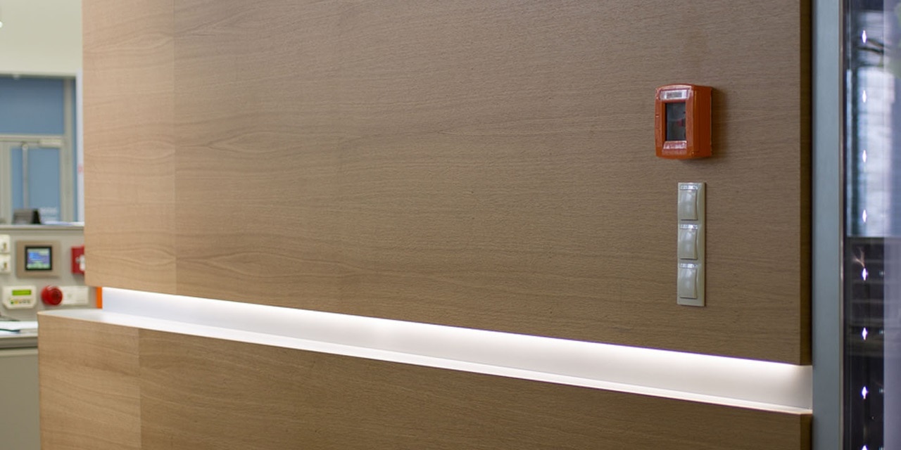 Modernes Bürointerieur mit LED-Lichtleiste, Feueralarm und elektrischen Lichtschaltern an der Wand