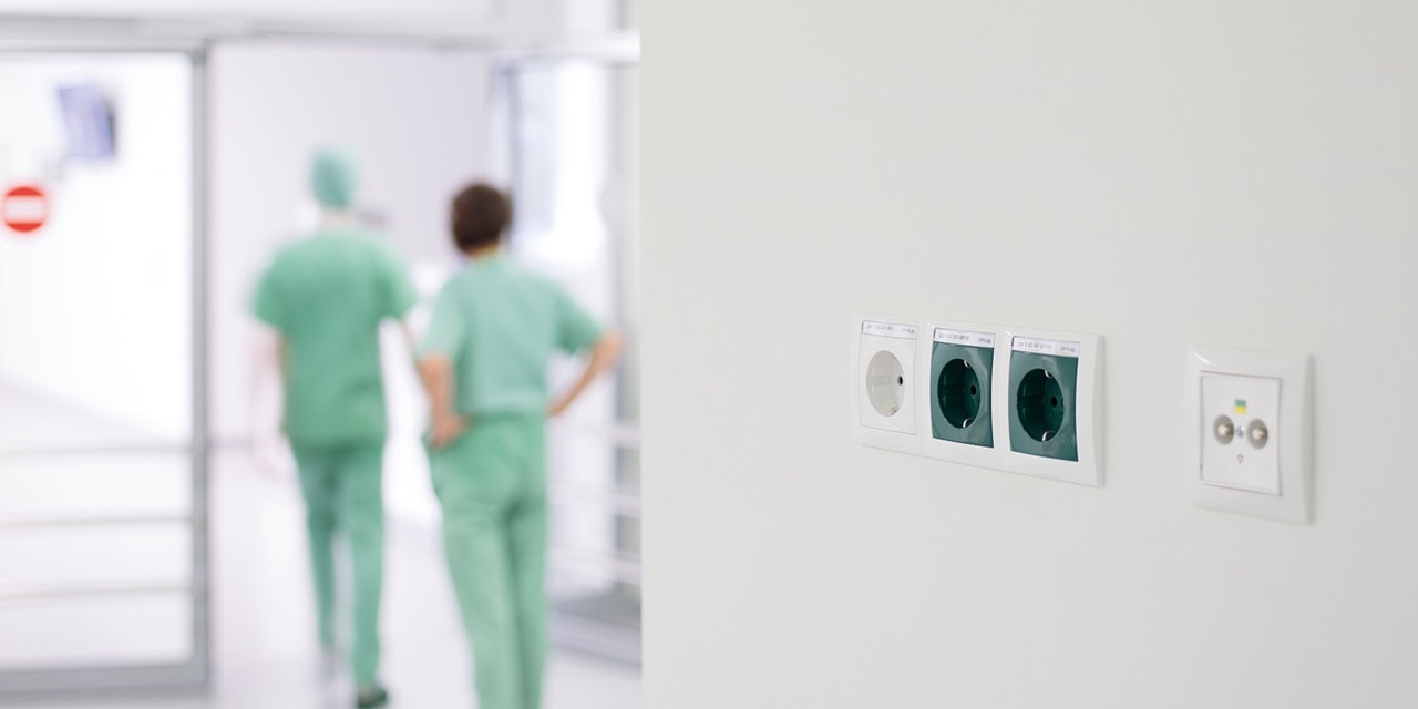 Krankenhausflur mit medizinischem Personal und Fokus auf Wandsteckdosen und Schalter