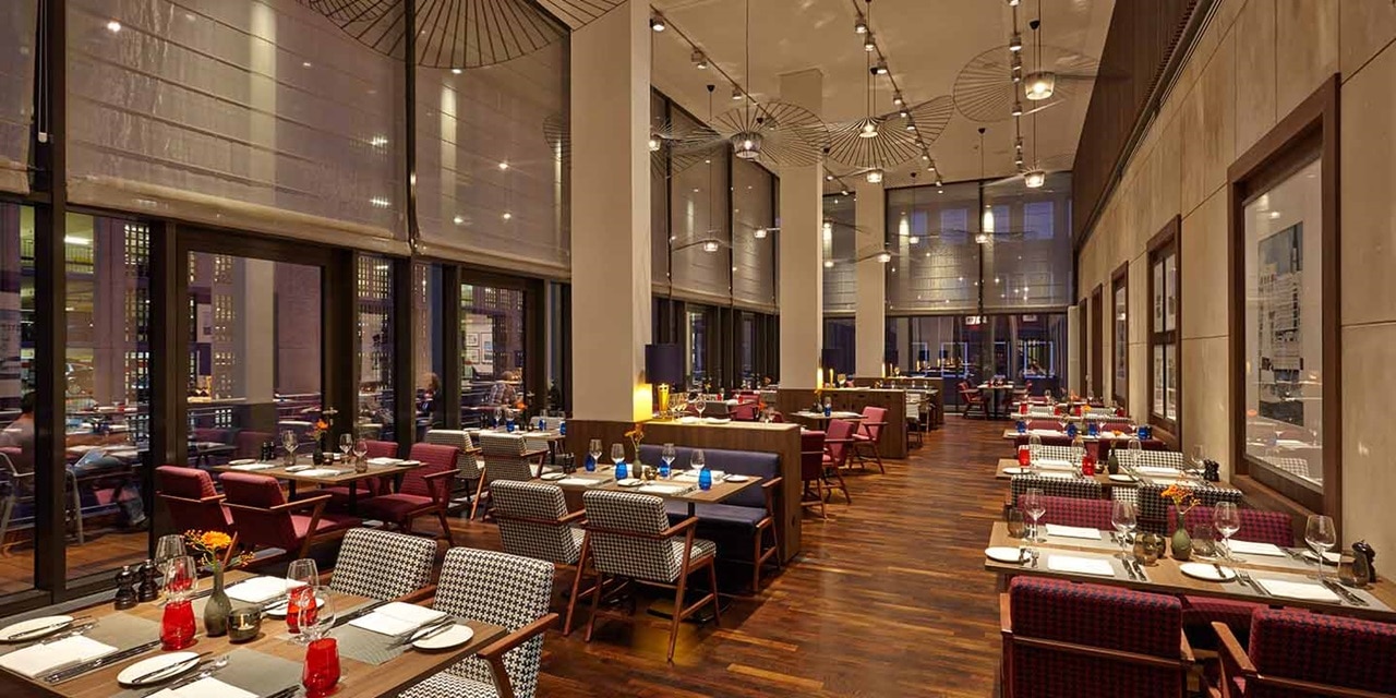 Elegantes Interieur eines modernen Restaurants mit gedeckten Tischen, Pendelleuchten und großen Fenstern in der Abenddämmerung