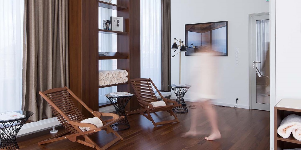 Unscharfe Gestalt geht an Holzliegestühlen in einem modernen Innenraum mit einer Wandleuchte vorbei