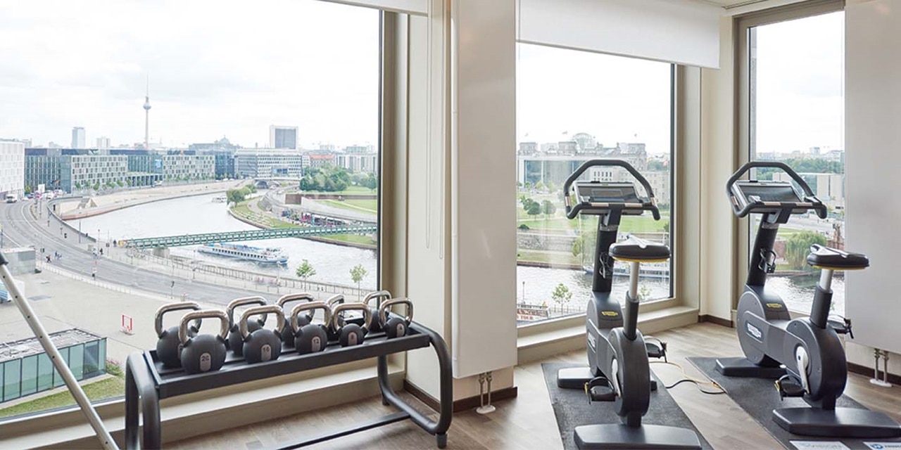 Fitnessstudio mit Trainingsgeräten und Blick auf eine Stadtsilhouette mit Fluss