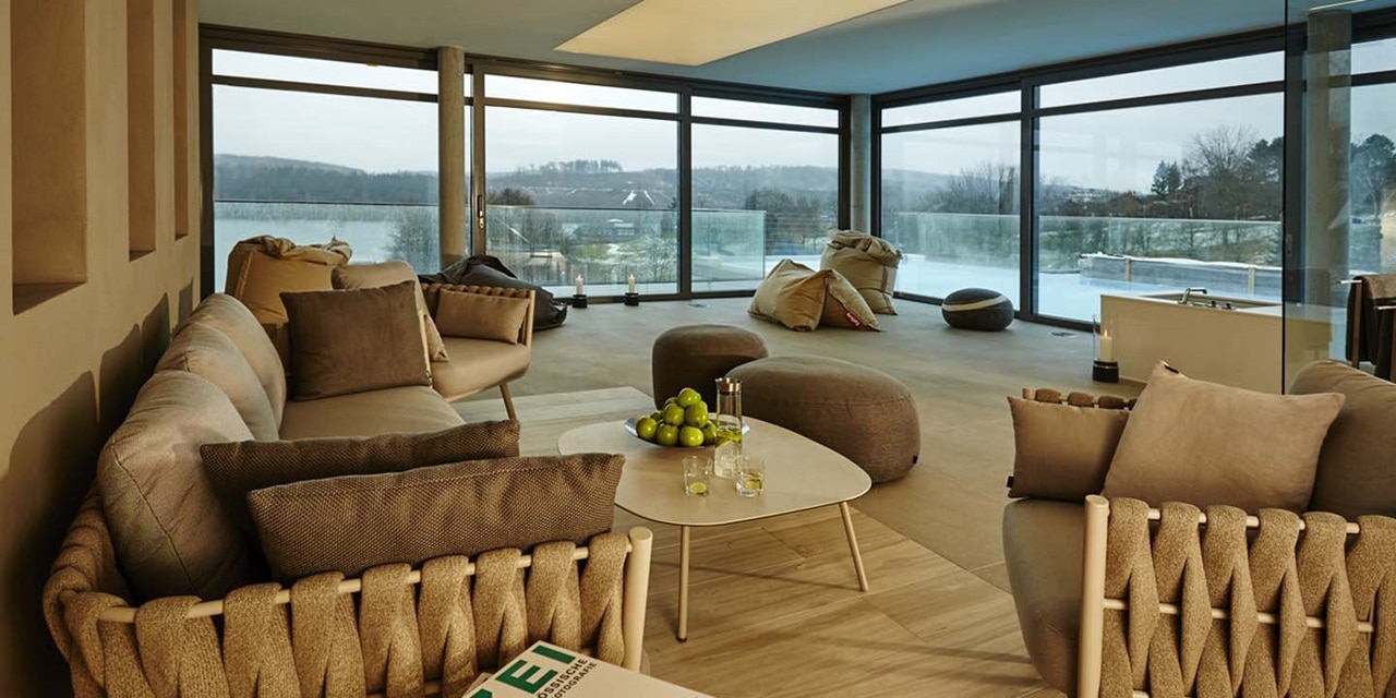 Modernes Wohnzimmerinterieur mit großen Fenstern mit Blick auf eine Winterlandschaft, warmen neutralen Farbtönen und bequemen Möbeln