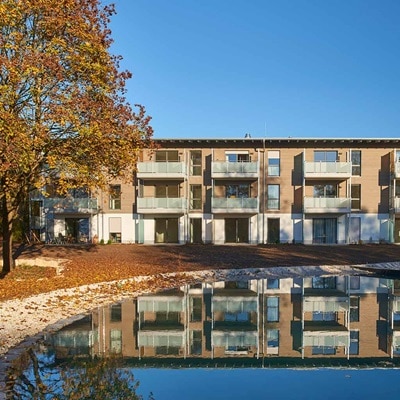 Modernes Wohngebäude mit Balkon, das sich an einem klaren Tag im Wasser spiegelt
