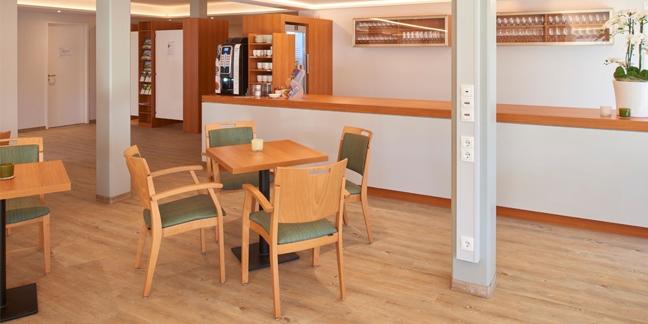 Modernes Cafeteria-Interieur mit Holztischen und Stühlen sowie einer Stromverteilungssäule mit mehreren Steckdosen