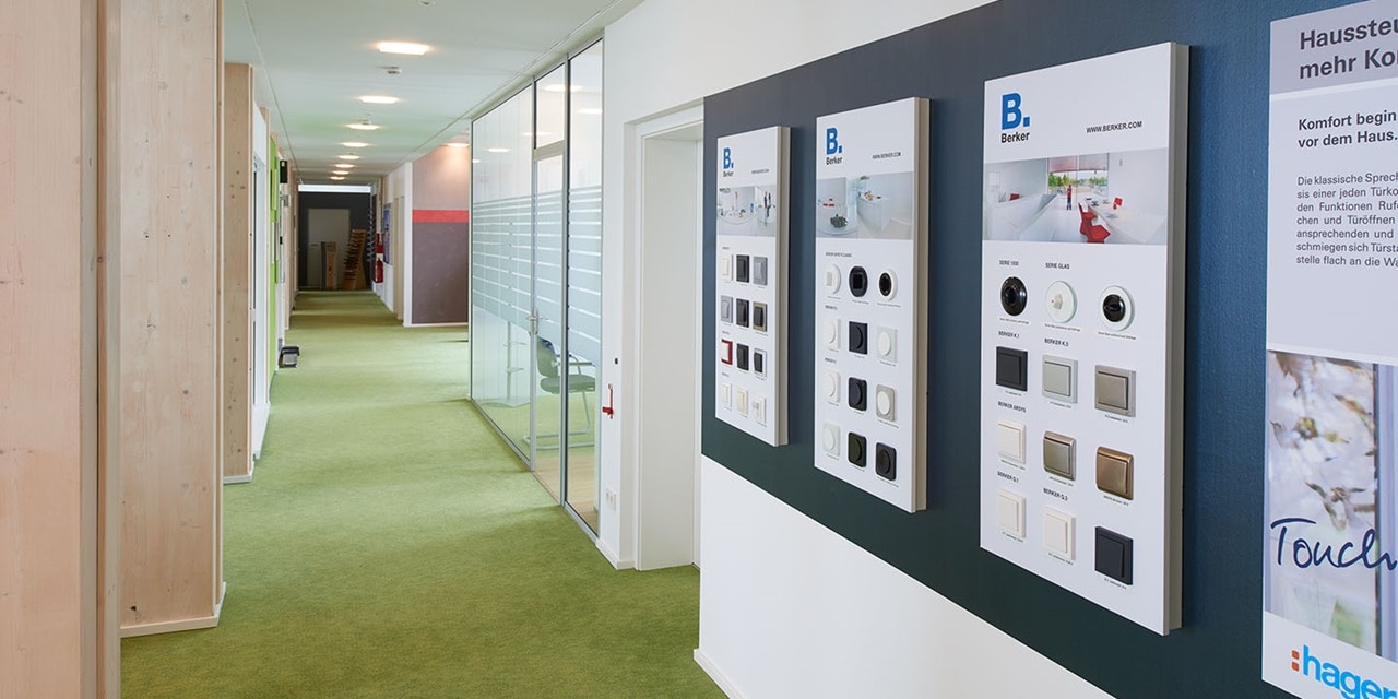 Ausstellung von Hager-Elektroschaltern und -systemen auf Displaytafeln in einem Flur mit grünem Teppich