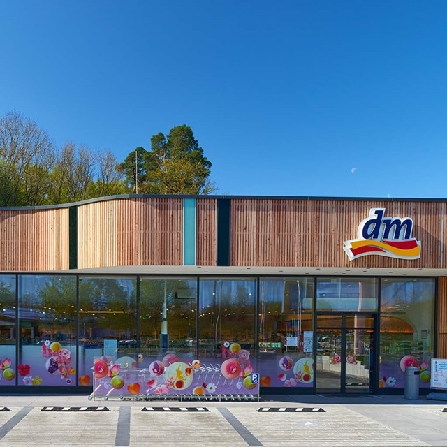 Außenansicht eines modernen Ladens mit großer Glasfront und Holzverkleidung, klarer Himmel.