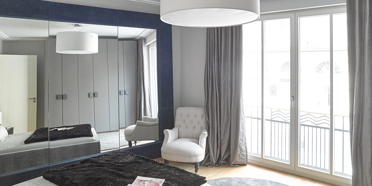 Modernes Schlafzimmerinterieur mit großer Pendelleuchte, Spiegelschranktüren und Balkontüren