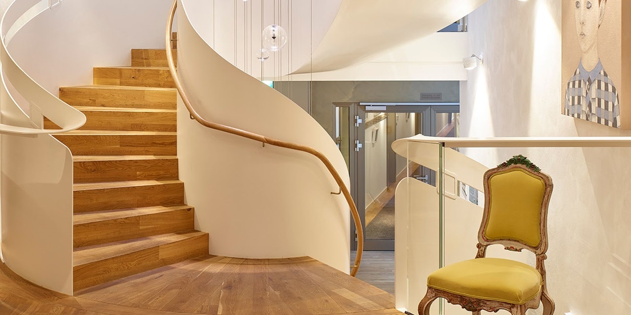 Spiralförmige Holztreppe in modernem Interieur mit eleganter Beleuchtung und einem Vintage-Stuhl