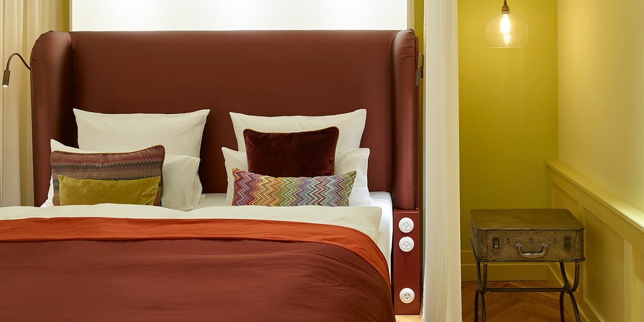 Modernes Schlafzimmerinterieur mit Bett, Kissen und hängender Lichtvorrichtung, mit an der Wand montierten Lichtschaltern.