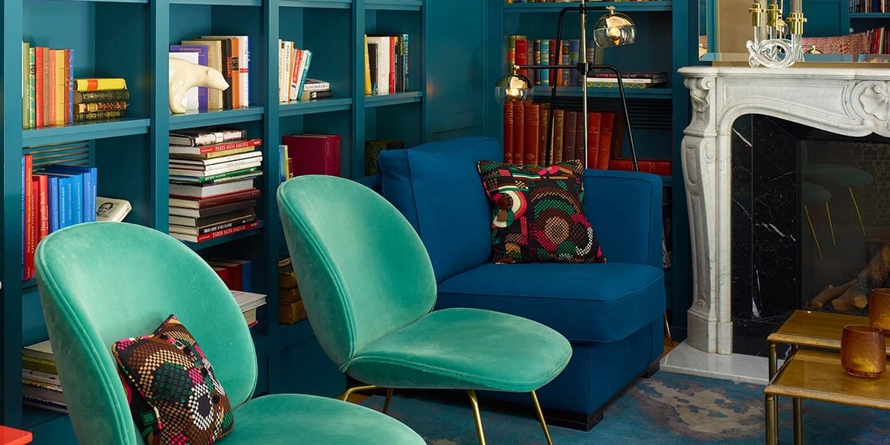 Elegantes Wohnzimmer im Vintage-Stil mit blauen Bücherregalen, grünen Samtsesseln und einer Messing-Stehlampe