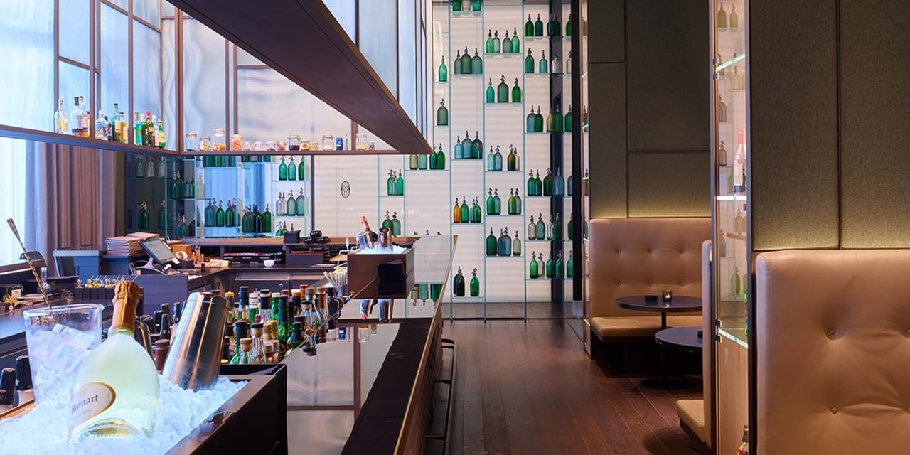 Modernes Bar-Interieur mit beleuchteten Regalen voller Flaschen, eleganter Sitzbereich und reflektierende Oberflächen