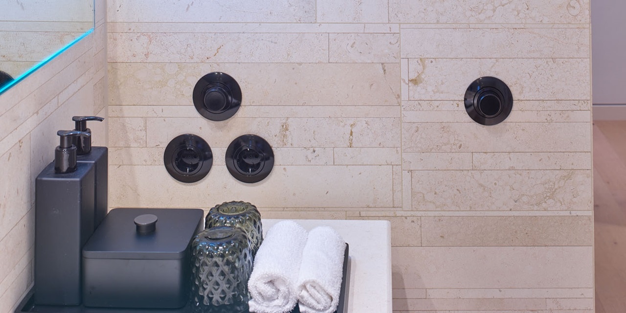Moderne schwarze Wandlichtschalter und Steckdosen an einer Steinfliesenwand mit Badezimmeraccessoires im Vordergrund