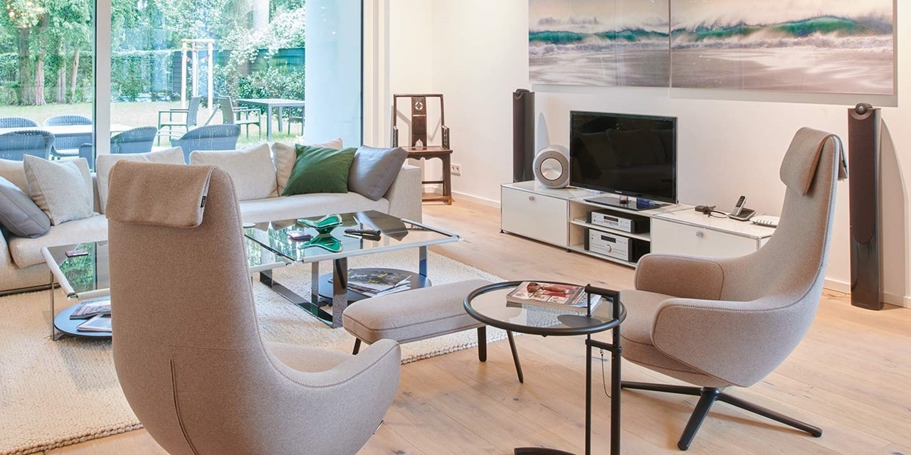 Modernes Wohnzimmer-Interieur mit bequemen Möbeln, großen Fenstern und Unterhaltungssystem inklusive Lautsprecher und Fernseher